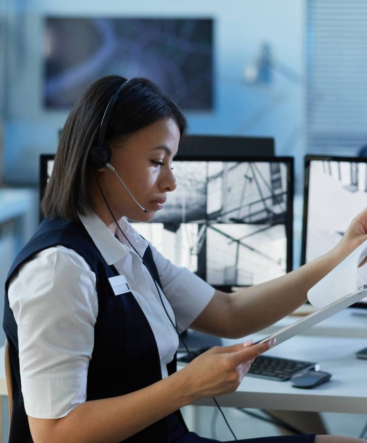 Side view portrait of young woman wearing headset in security center office with surveillance camera feeds in background